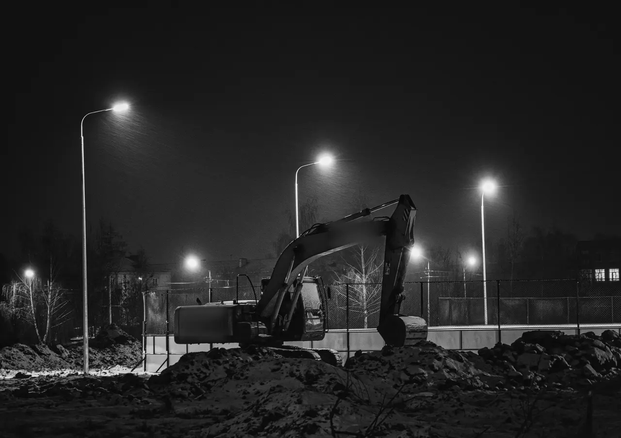 Gece sokak lambaları altında hafriyat sahasında bekleyen ekskavatör